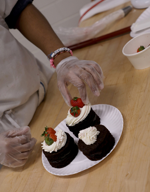 Image of a person's hands arranging strawberries on a frosted pastry