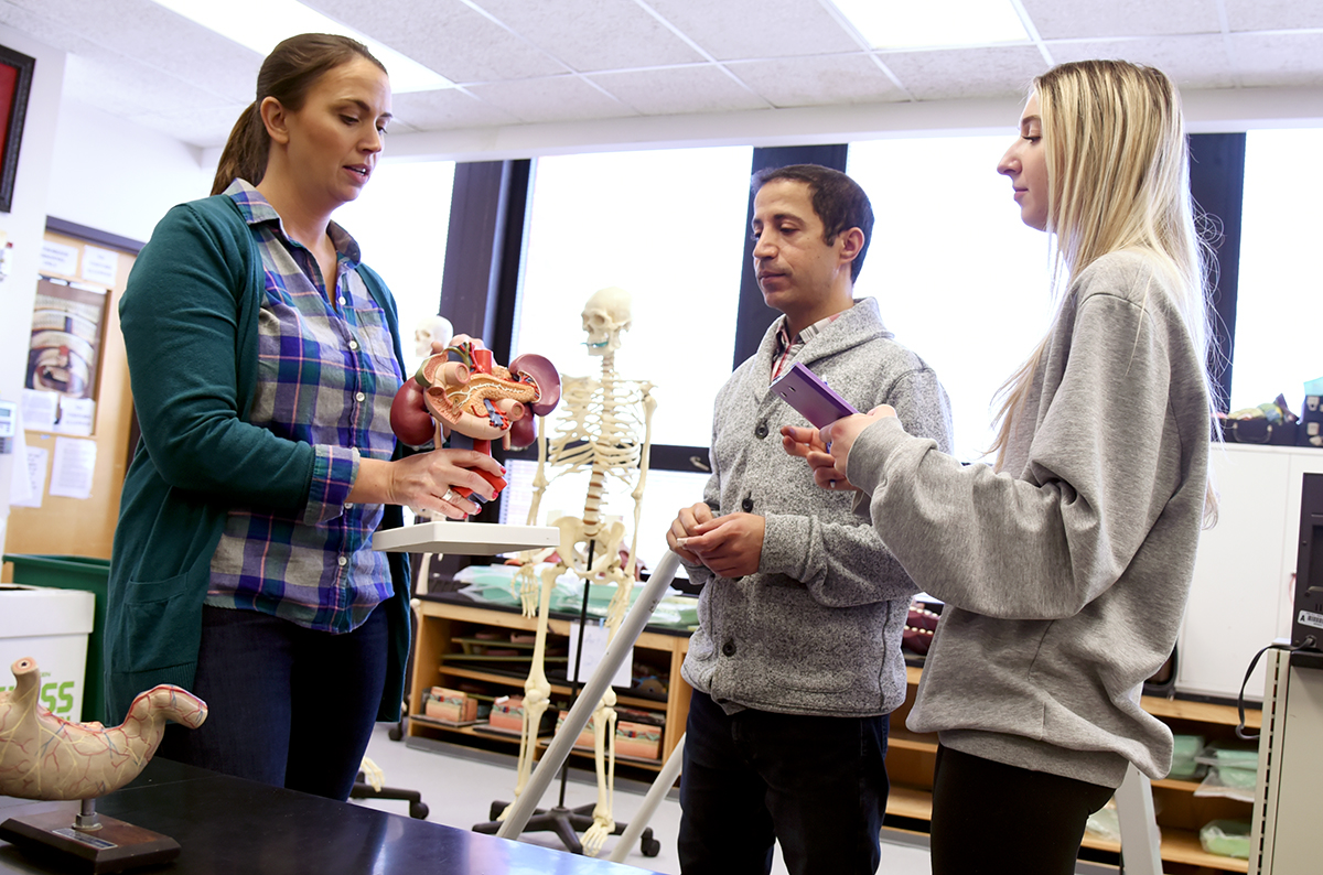 Image of three people in classroom, instructor showing two students model of digestive system