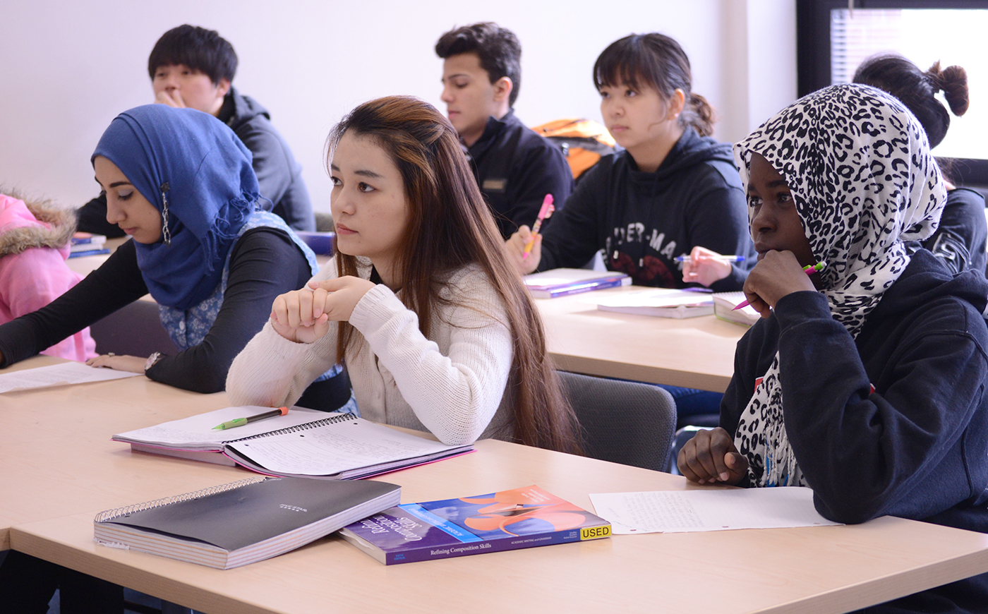 Students sitting in classroom with notebooks and pens, listening