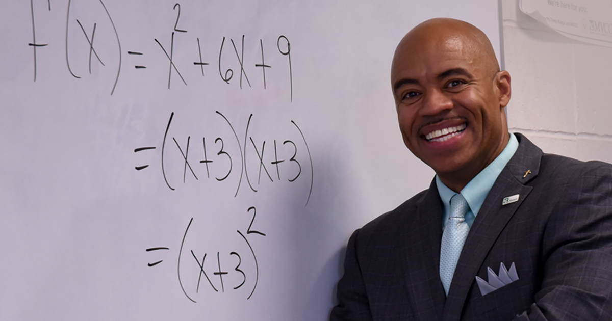 Image of MVCC alumnus Musco Millner III standing in classroom with mathematical formula on board