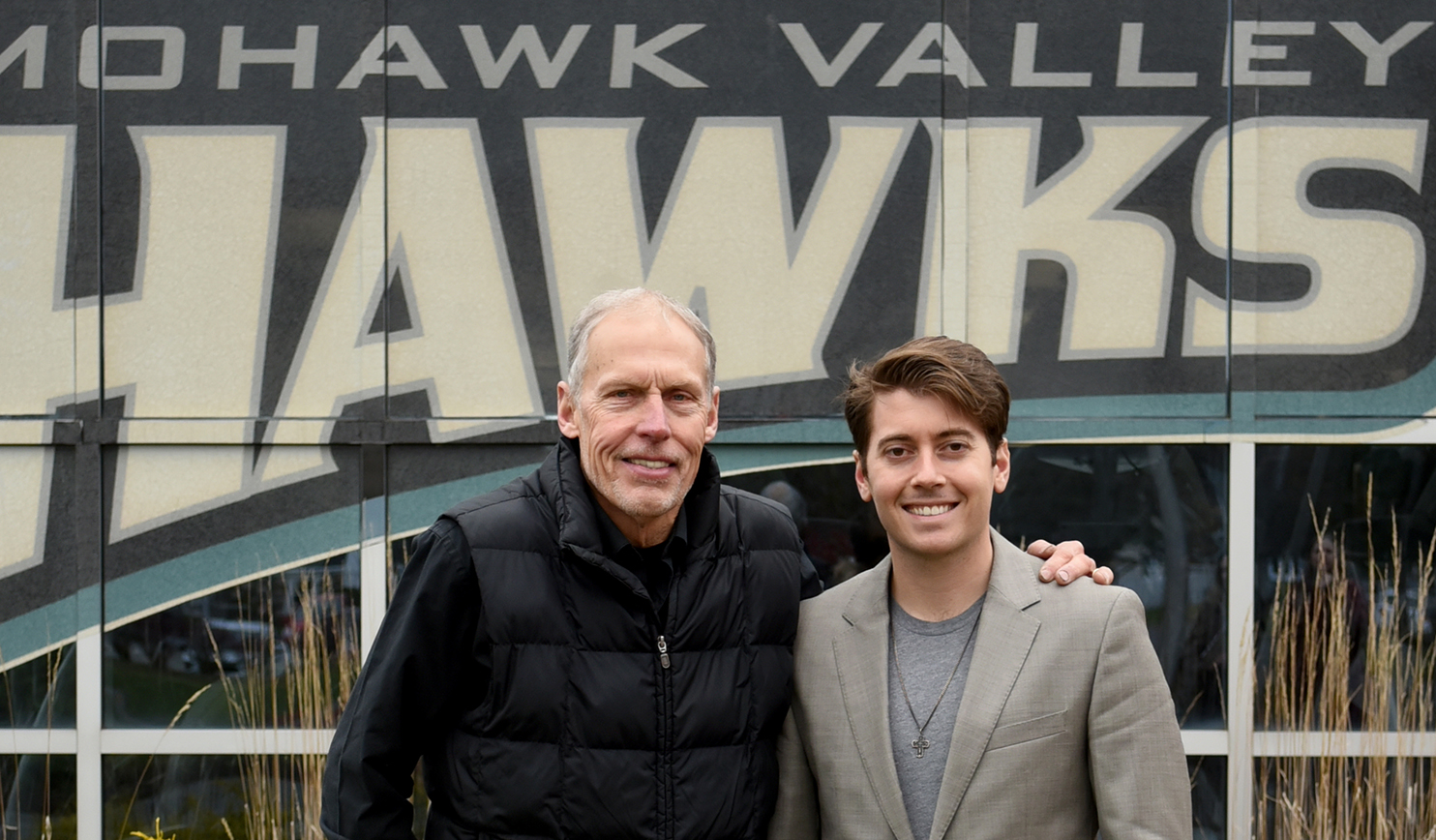 Coach Gould and son David stand in front of Hawks logo on building 