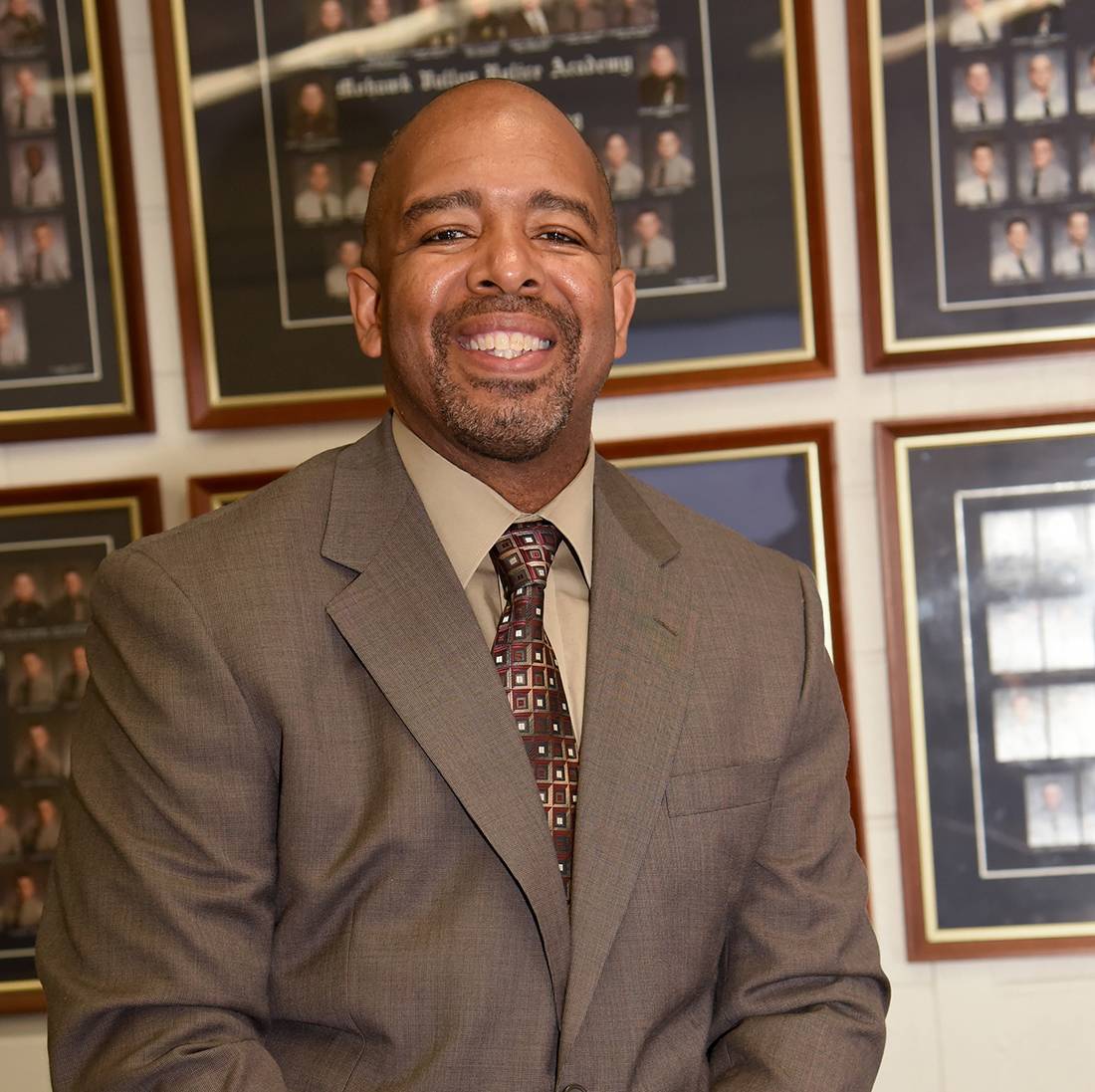 image of Troy Little smiling, in front of photos of law enforcement graduates