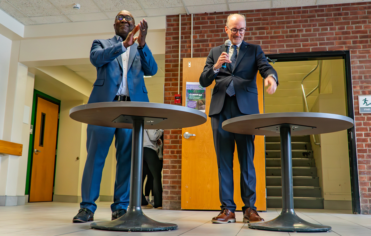 Two people standing at tables making an announcement